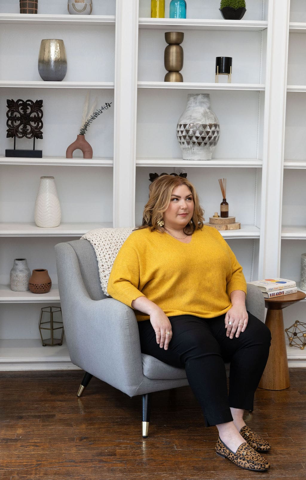 Trauma and grief healing practitioner sitting in front of bookshelf looking off into the distance