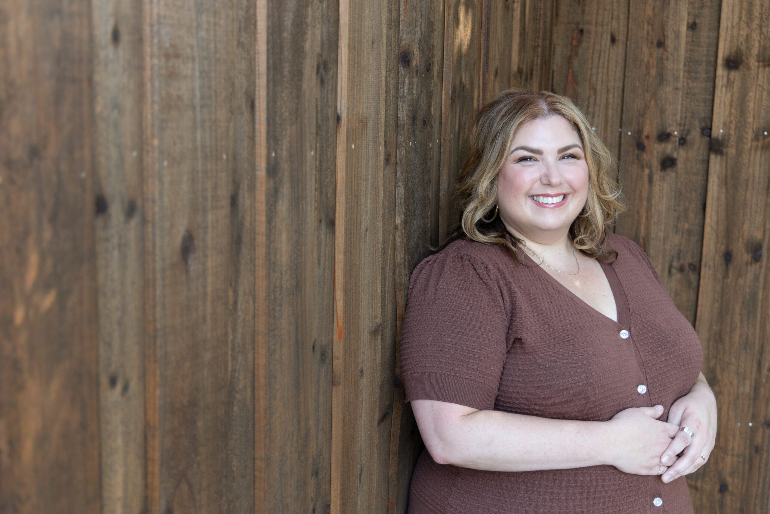 Somatic healing practitioner leaning against a fence and smiling at the camera