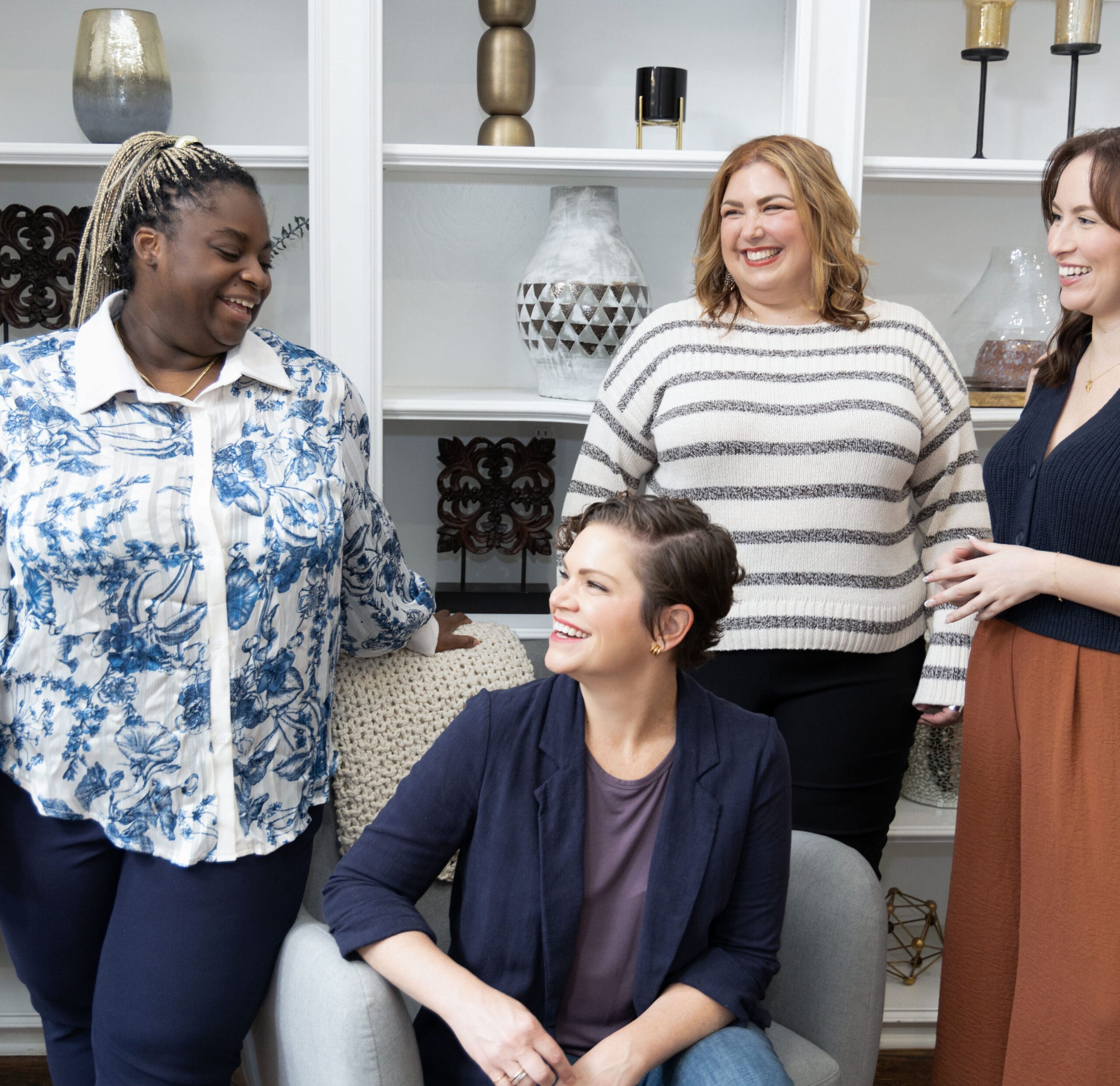 Two somatic coaching providers talking and laughing with other therapists in front of a bookshelf.