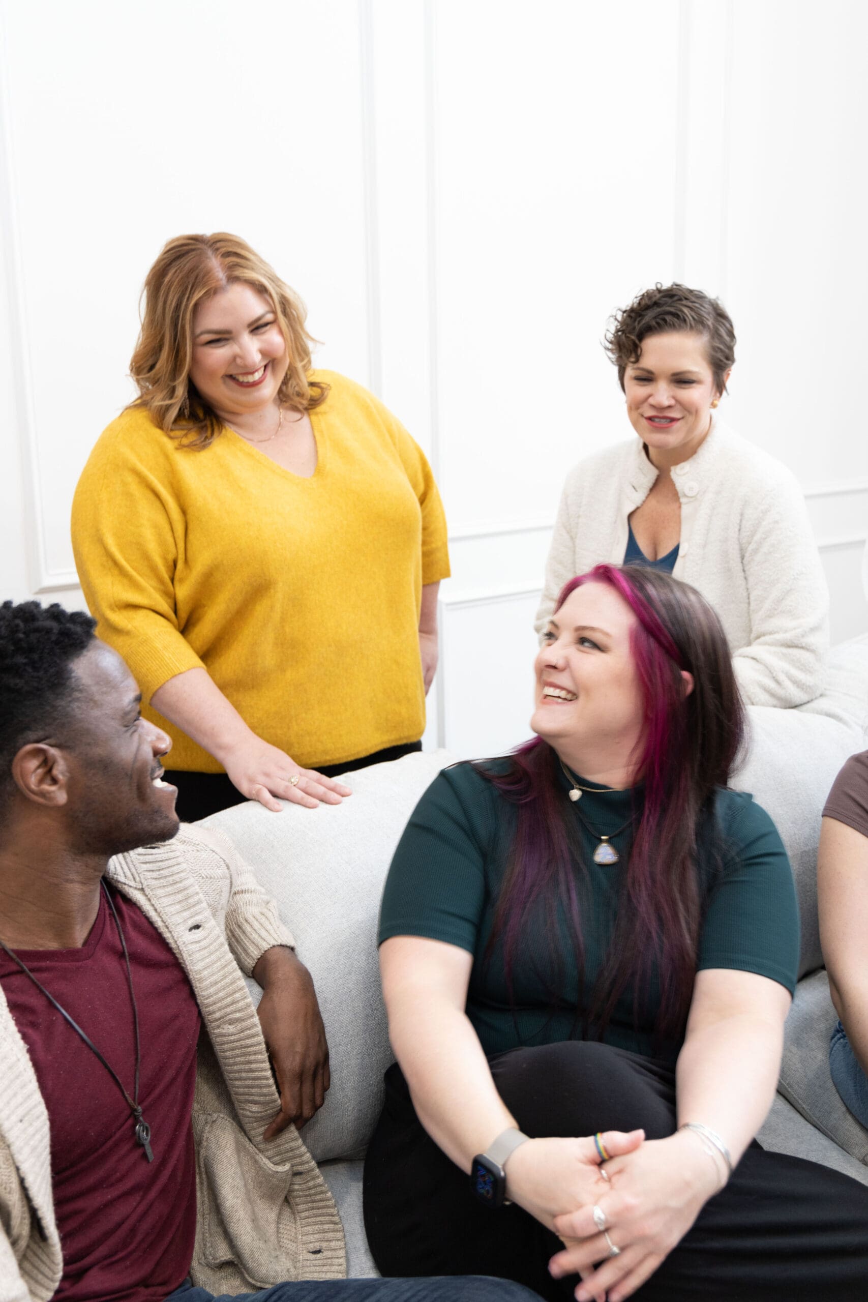 Somatic coaches and trauma therapists sitting on couch smiling and laughing with one another.