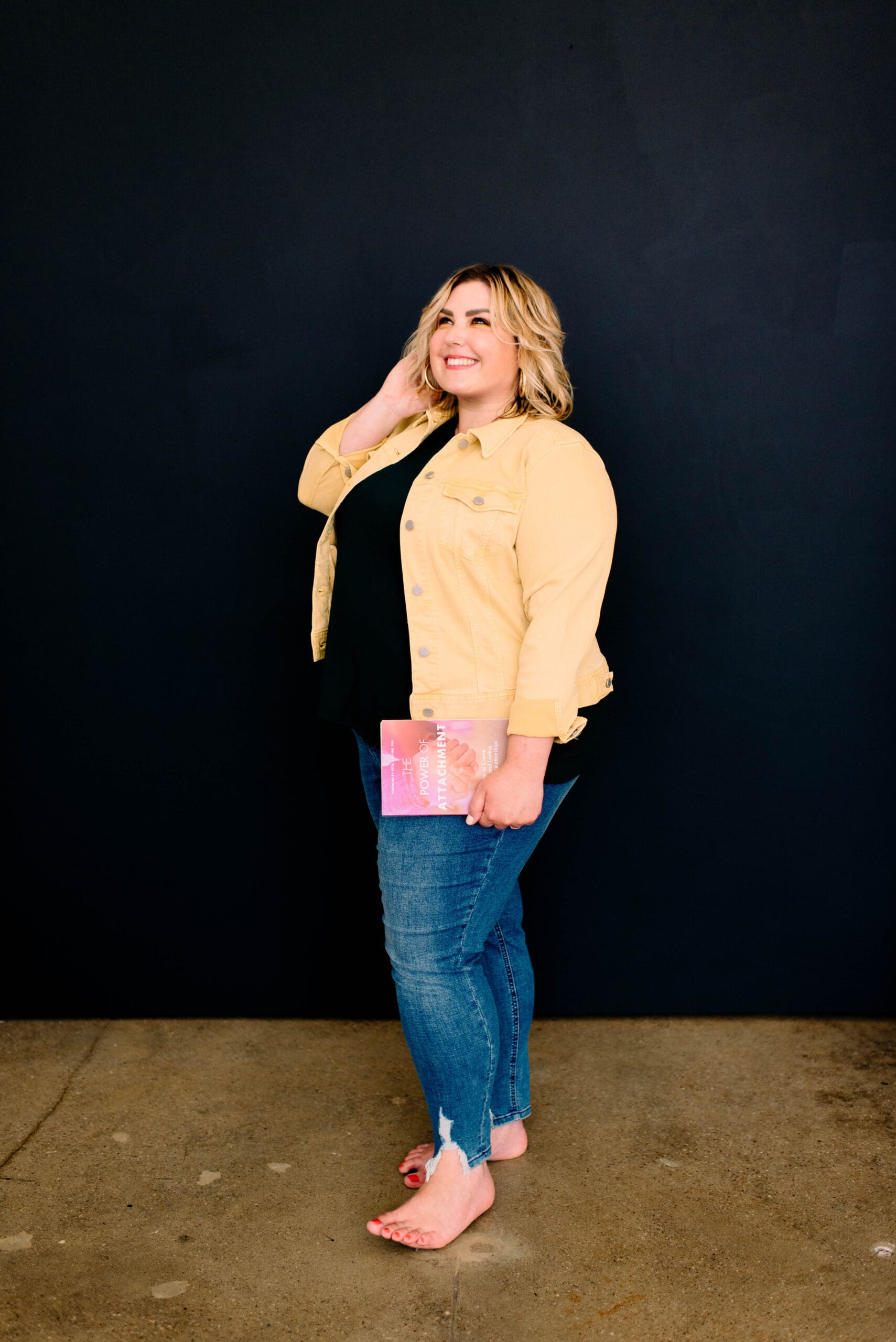 Somatic healing practitioner standing and holding a book, smiling off into the distance