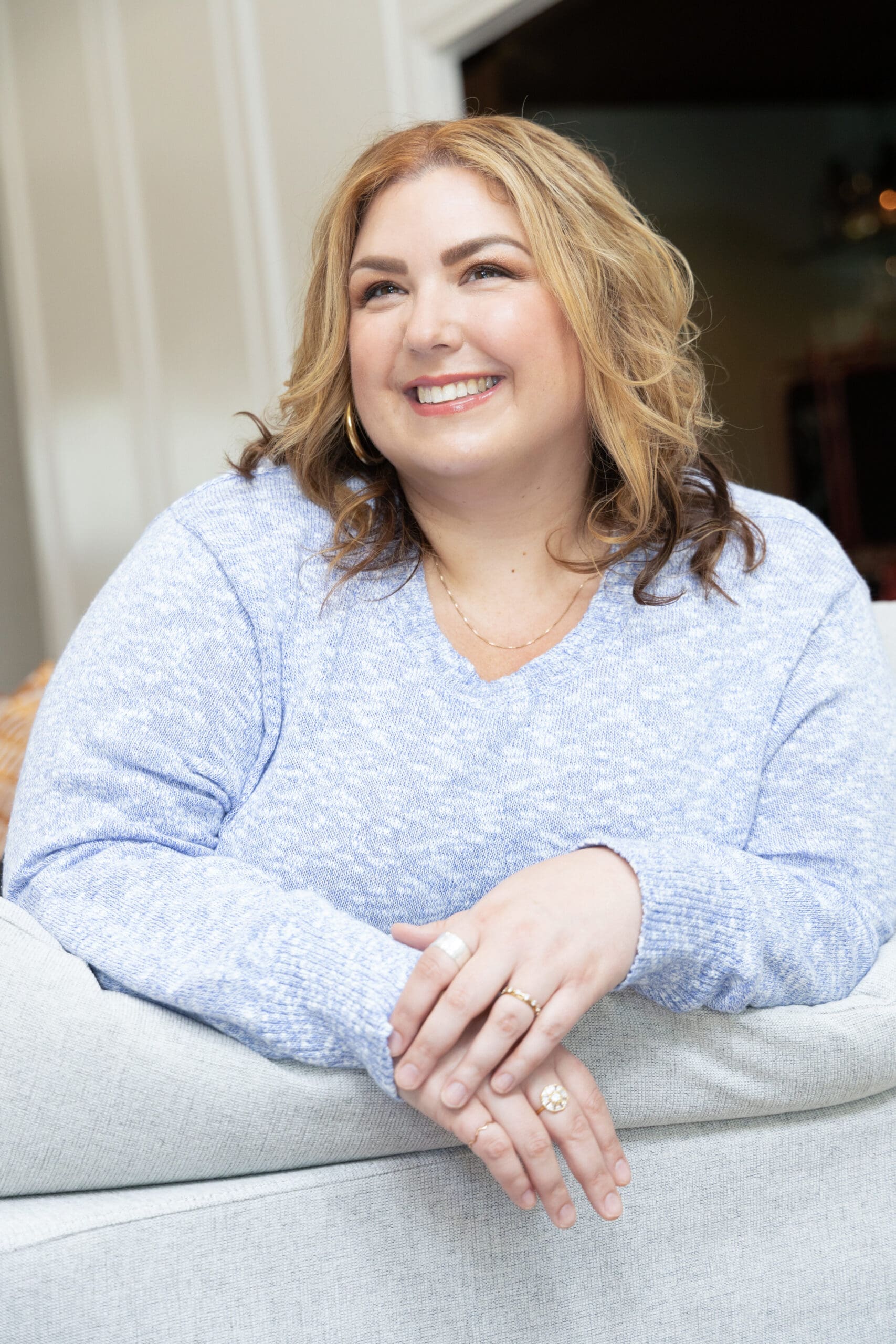 Therapist mentor and somatic healing practitioner leaning on couch and smiling off into the distance.