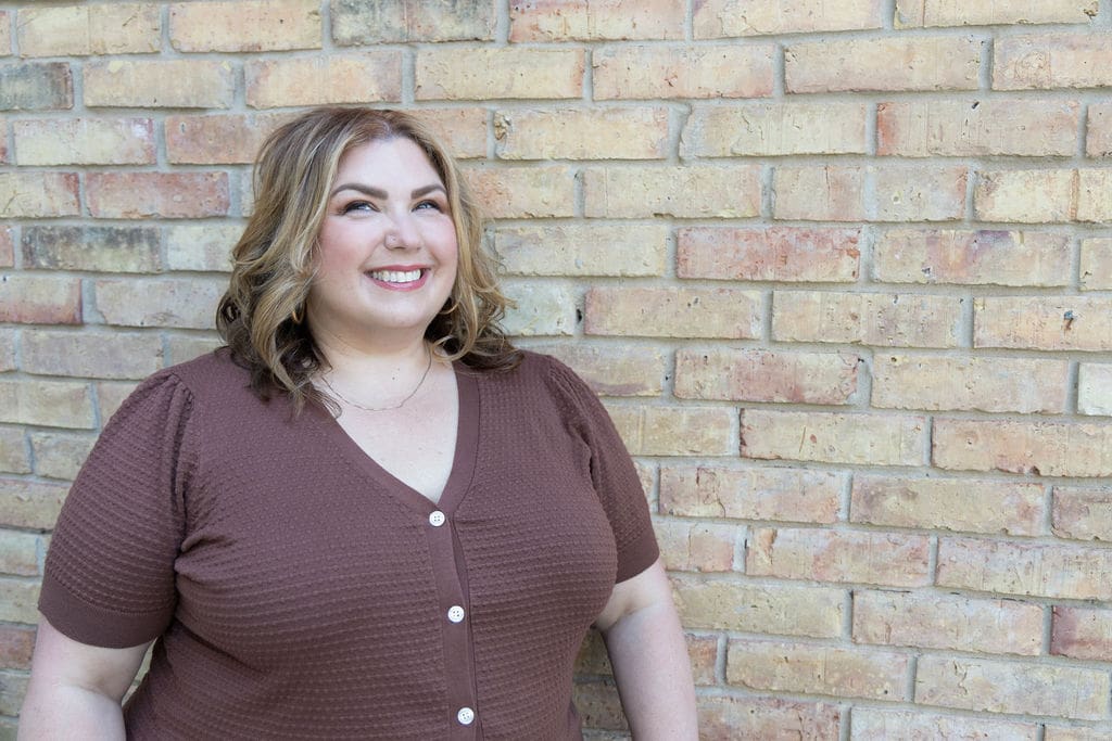Therapist mentor and somatic experiencing practitioner standing in front of a brick wall and smiling off into the distance.