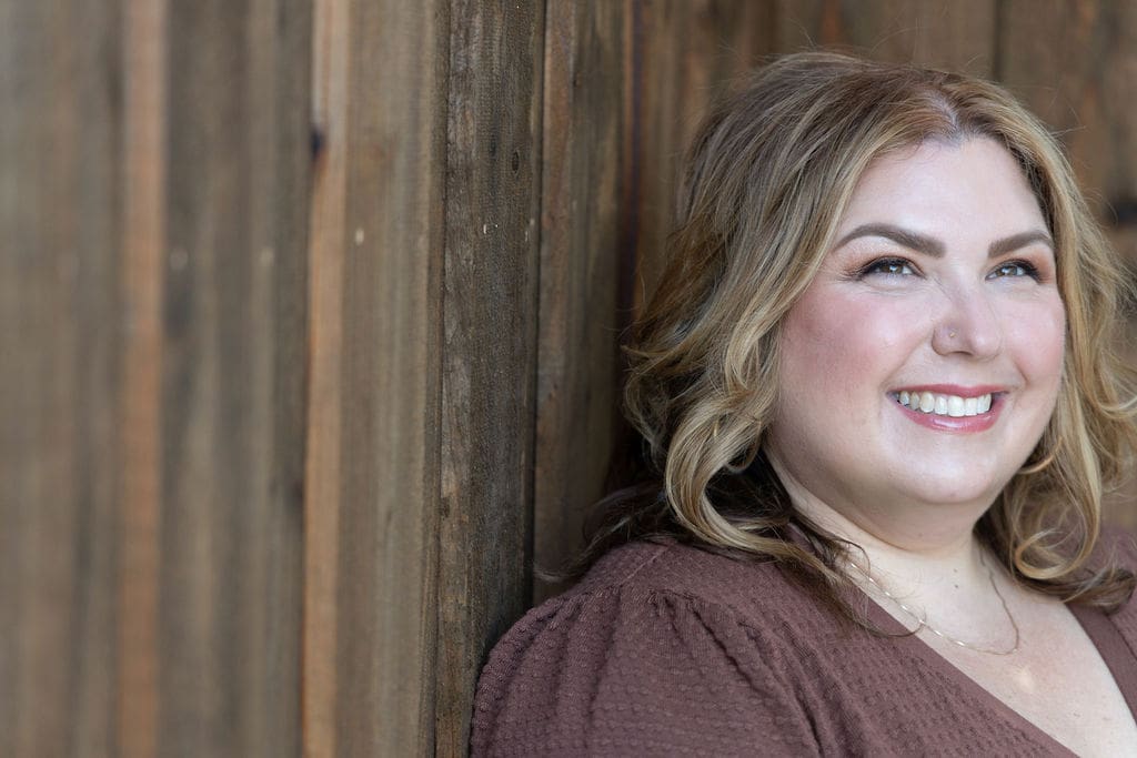 Therapist mentor and somatic healing practitioner wearing a brown shirt standing in front of a fence and smiling off into the distance.