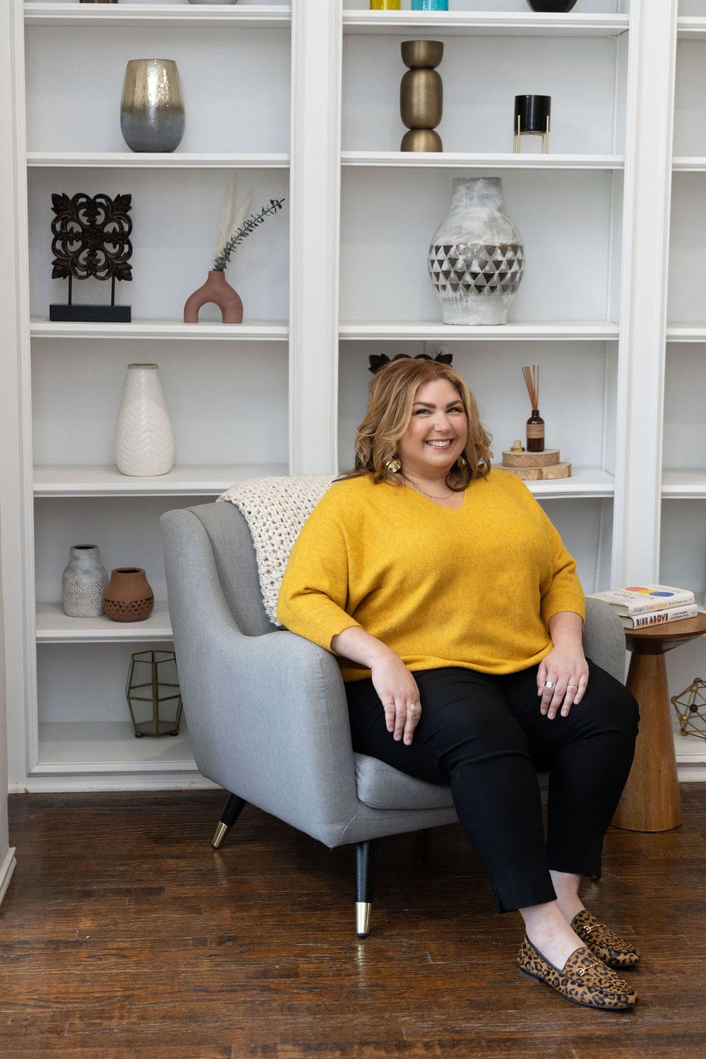 Therapist mentor and trauma healing practitioner sitting in front of bookshelf in yellow shirt and smiling off into the distance