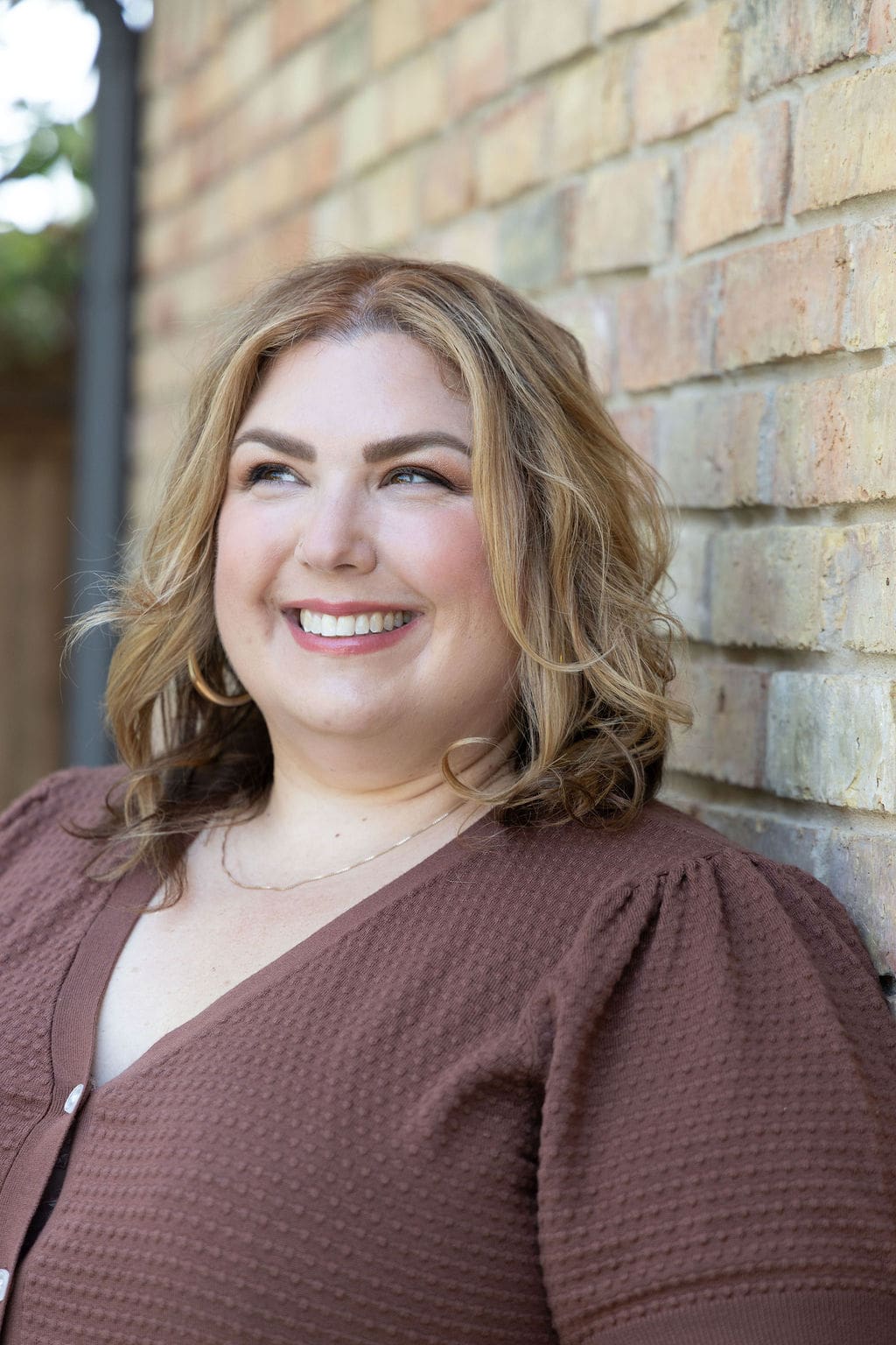 Therapist mentor and somatic experiencing practitioner standing in a brown shirt against a brick wall and smiling off into the distance.
