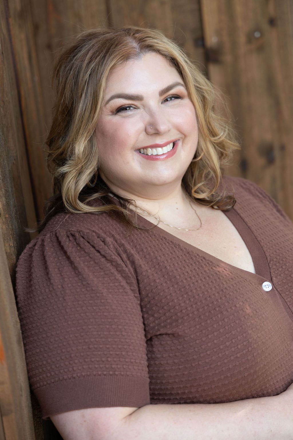 Somatic experiencing practitioner and therapist mentor standing against a brown fence in a brown shirt and smiling at the camera.