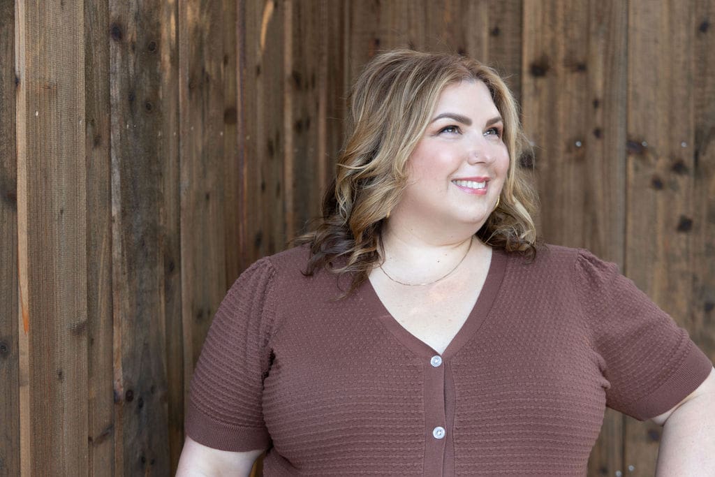 The Empowered Therapist and somatic experiencing practitioner standing in front of a fence in a brown shirt, smiling off into the distance.