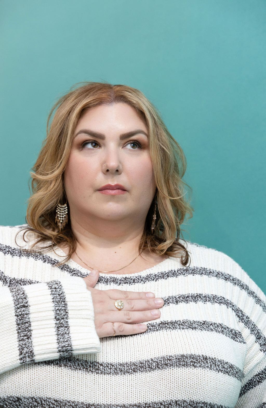 The Empowered Therapist wearing a striped sweater in front of a teal background, holding her hand over her heart and gazing off into the distance.