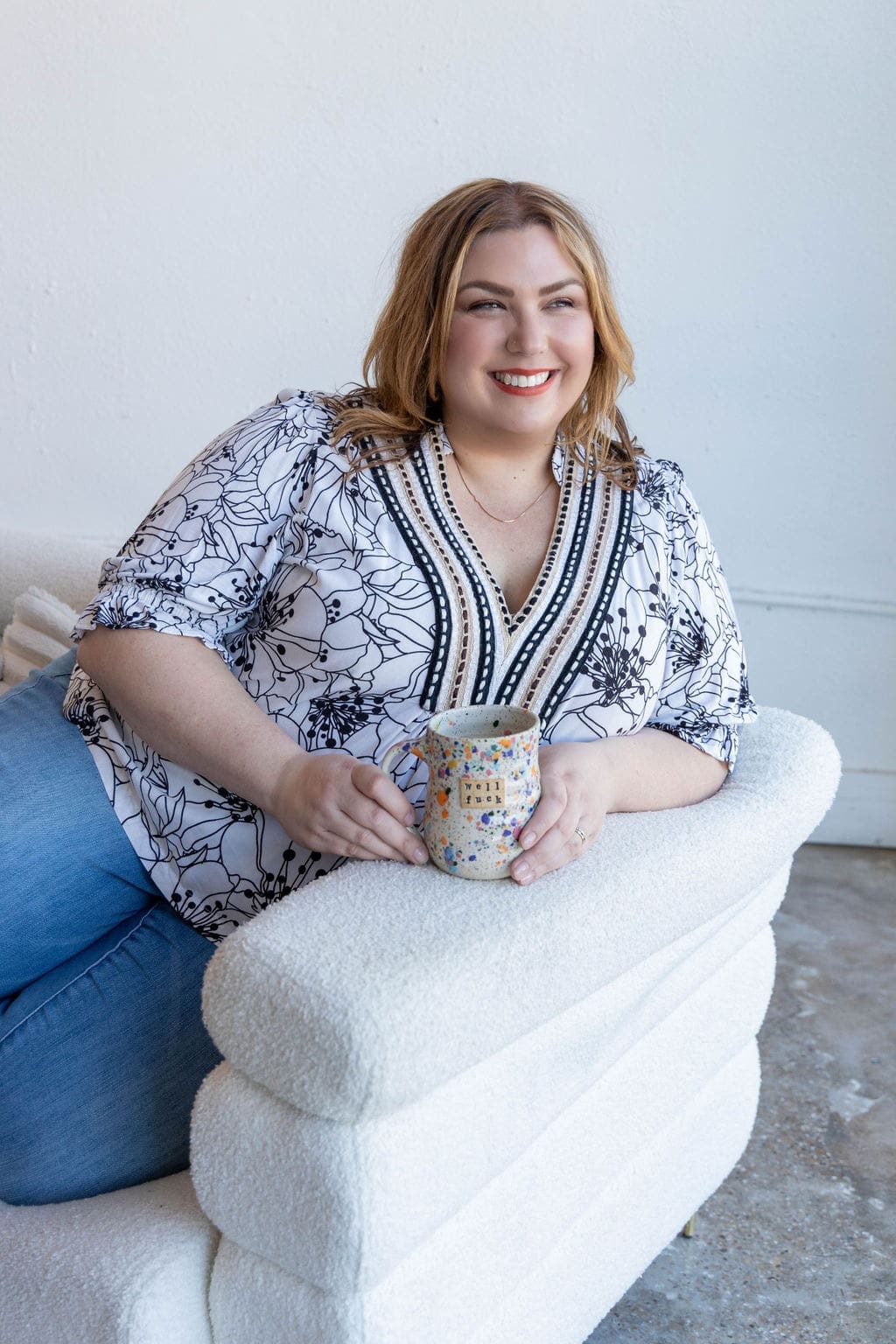 Therapist mentor sitting on a couch holding a mug and smiling off into the distance.
