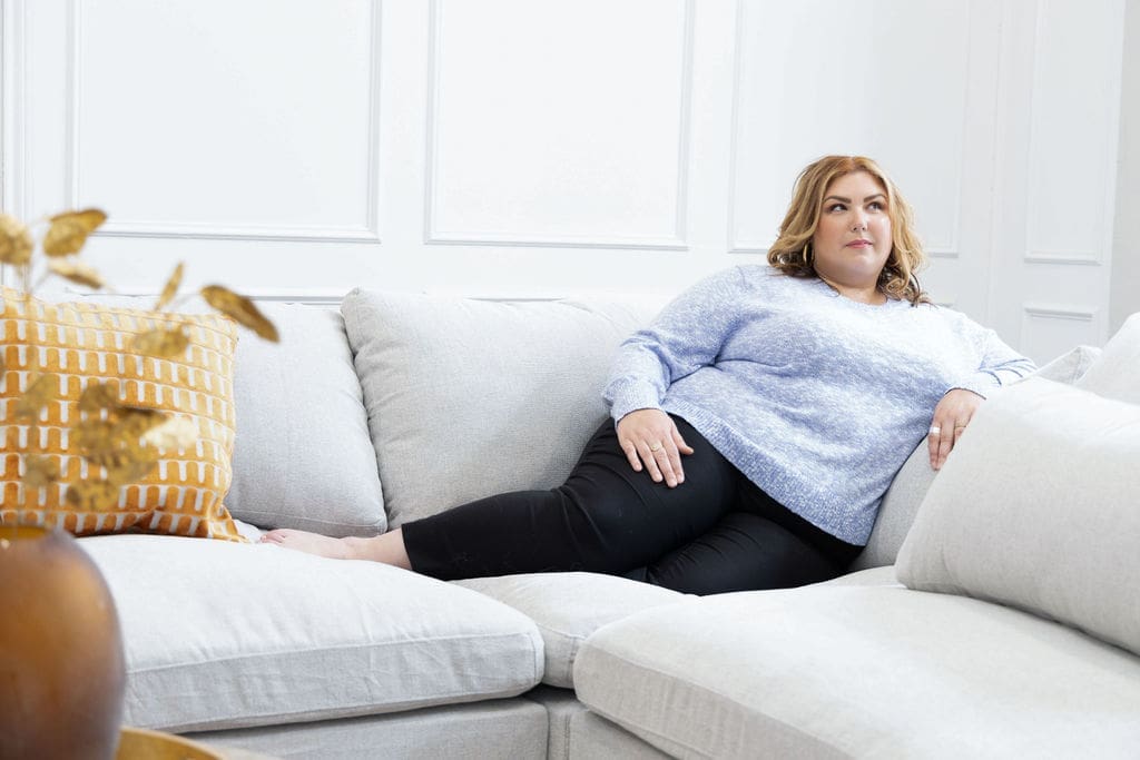 Somatic experiencing practitioner and trauma healing expert laying on a gray couch and looking out into the distance