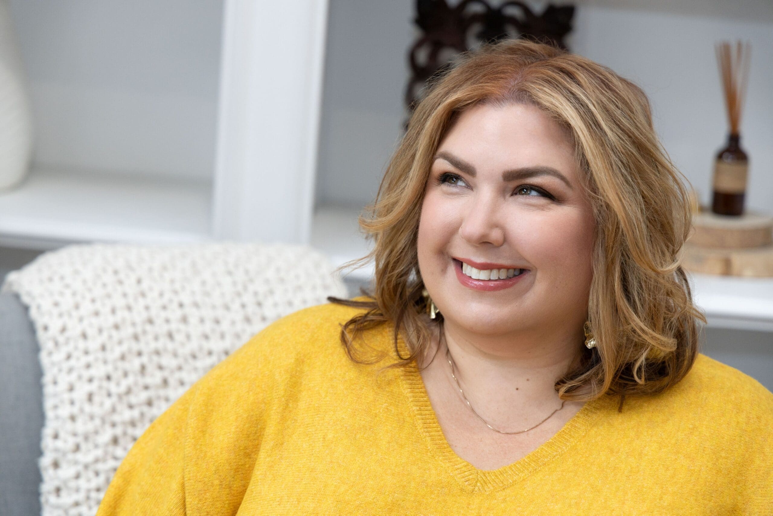 The Empowered Therapist and therapist mentor wearing a yellow shirt in front of a bookshelf and smiling off into the distance.