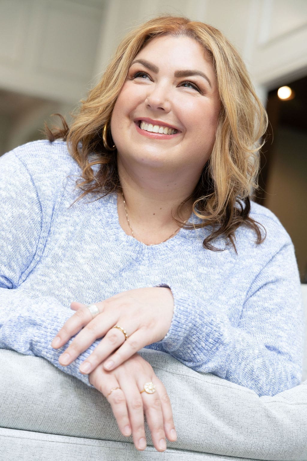 Therapist mentor and somatic experiencing practitioner leaning on the arm of a couch in a blue shirt, smiling off into the distance.