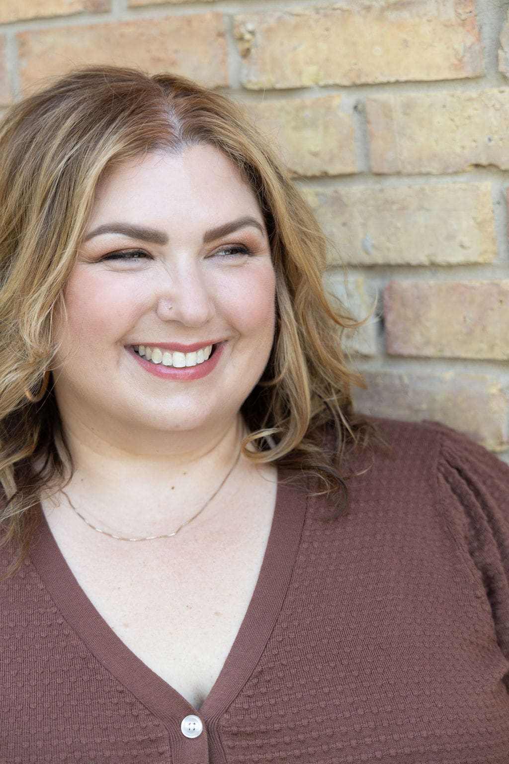 Therapist mentor and somatic experiencing practitioner standing against a brick wall in brown shirt, smiling off into the distance.