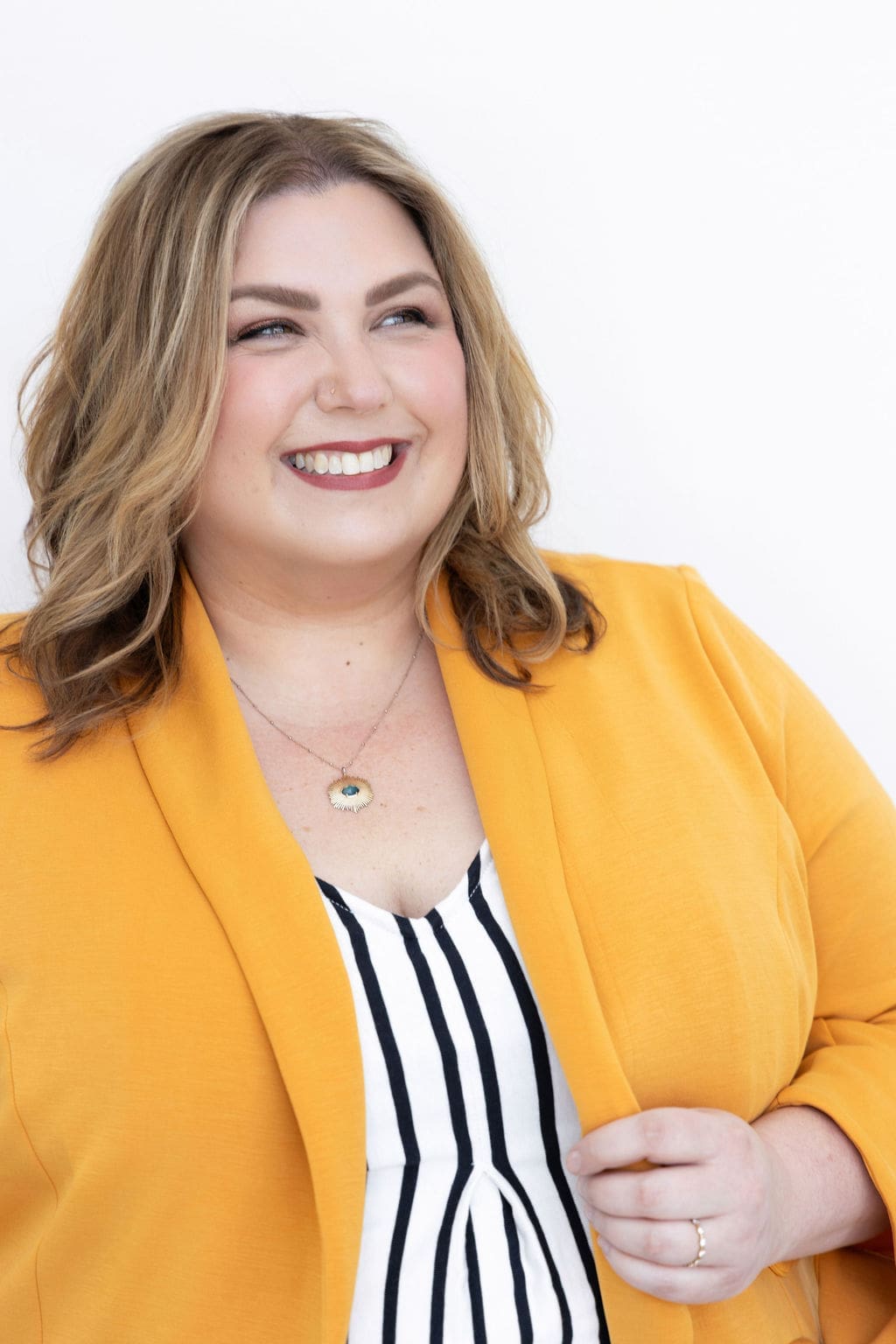The Empowered Therapist and therapist mentor wearing a striped shirt and yellow jacket, smiling off into the distance.