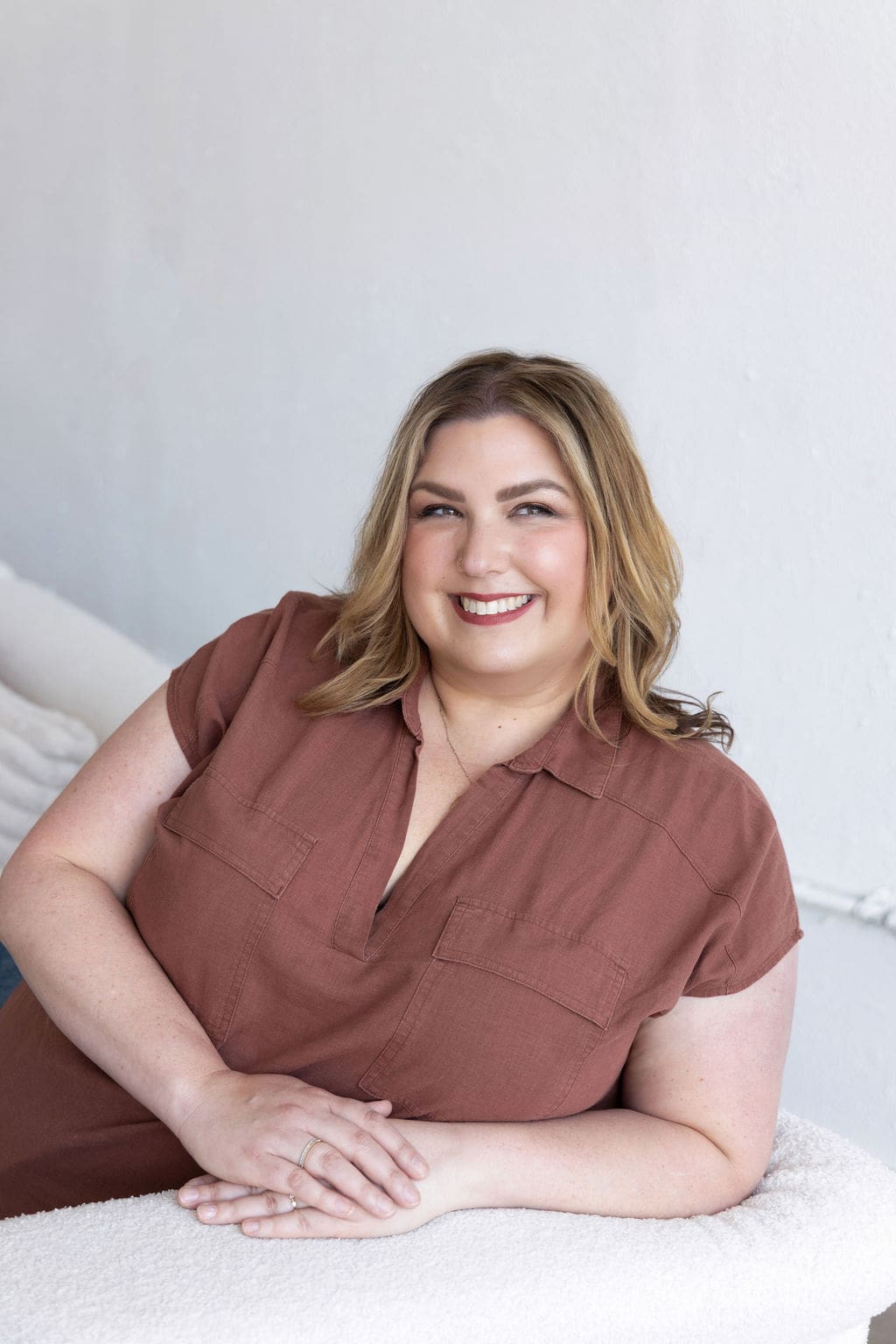 The empowered therapist and therapist mentor sitting on a white couch in a brown shirt, smiling off into the distance.
